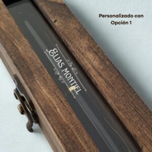 Vista detallada del grabado láser 'Elias Montiel' sobre la ventana de acrílico del estuche de madera, mostrando la Opción 1 de personalización.