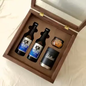 Una vista aérea del estuche de madera abierto, mostrando las dos cervezas Tecate Light, el portacervezas con el nombre "Adalberto" grabado y un frasco de botana.